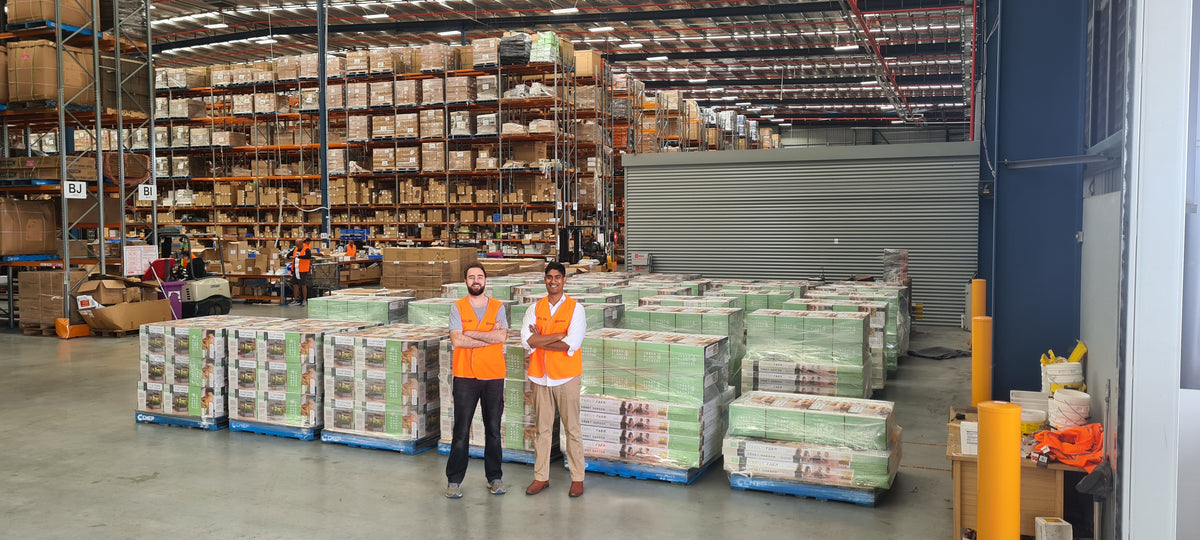Dilhan and Peter standing in front of pallets of boxed indoor gardens in the Costco warehouse